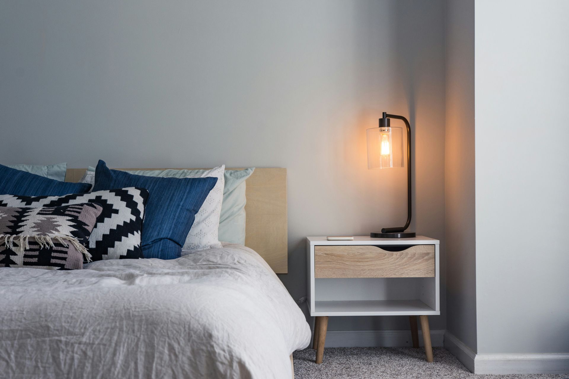 A bedroom with a bed , nightstand and lamp.