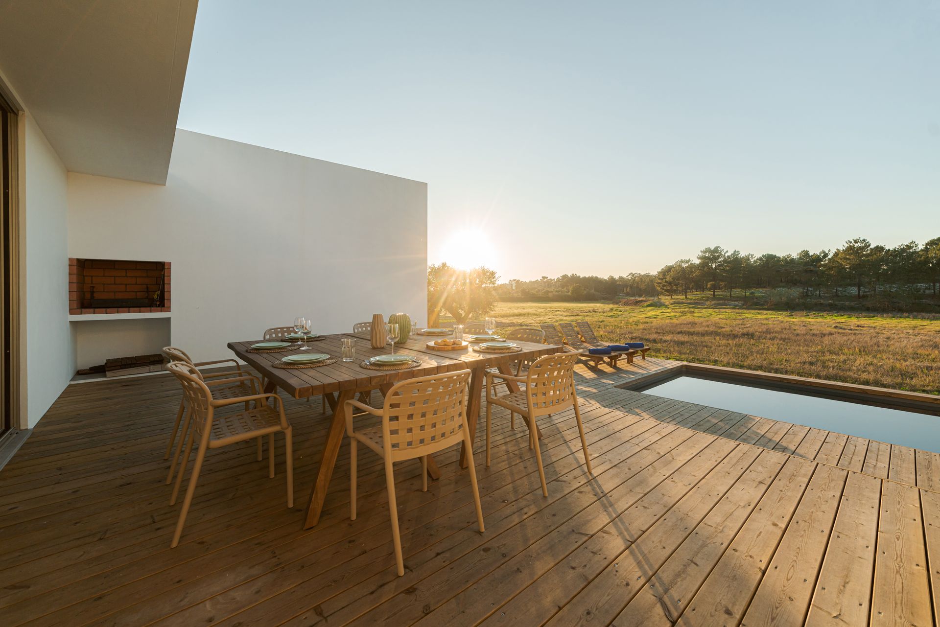 A wooden deck with a table and chairs next to a swimming pool.