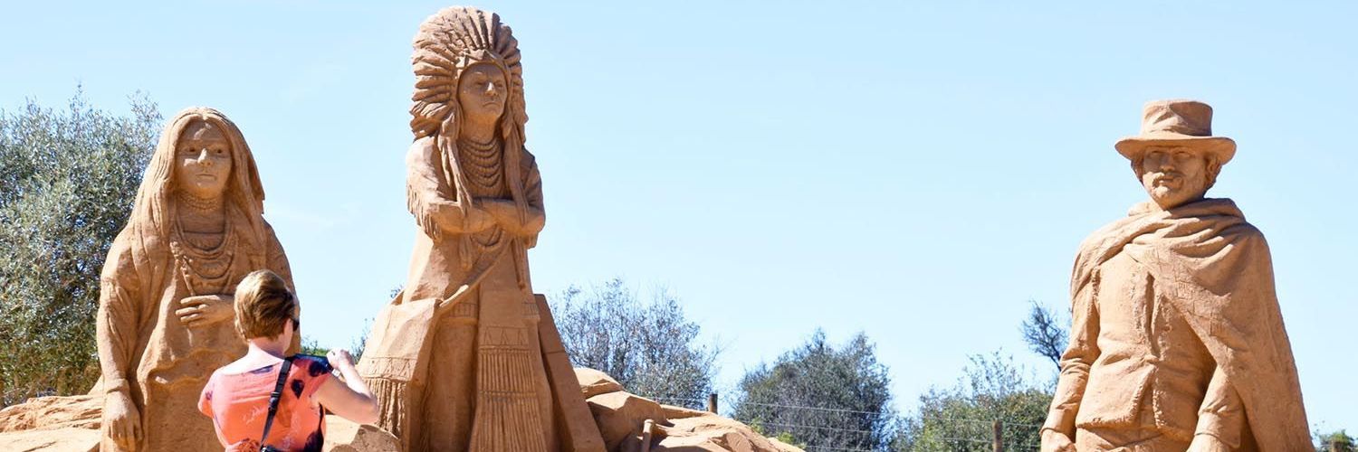 A man and two women are standing next to each other in front of a sand sculpture.