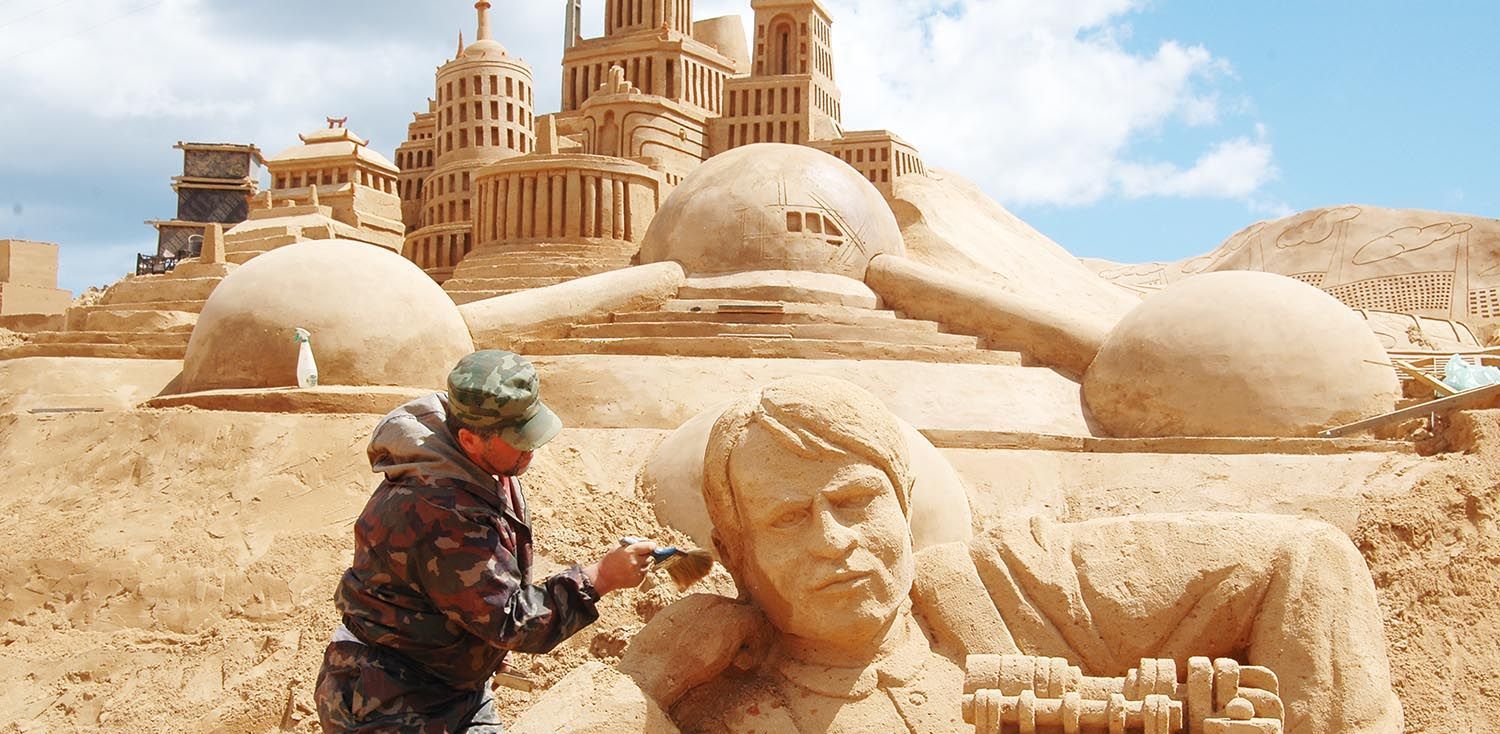 A man is working on a sand sculpture in front of a castle.