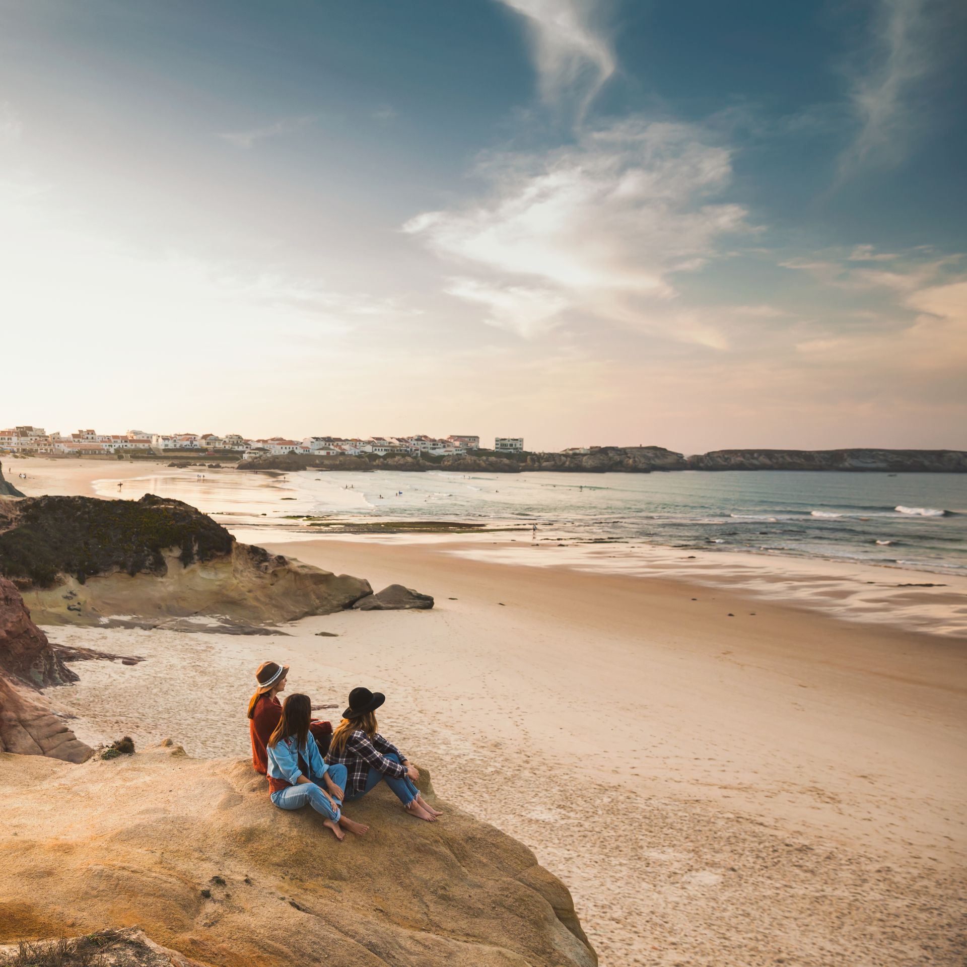 A group of people are sitting on a rock on a beach looking at the ocean.