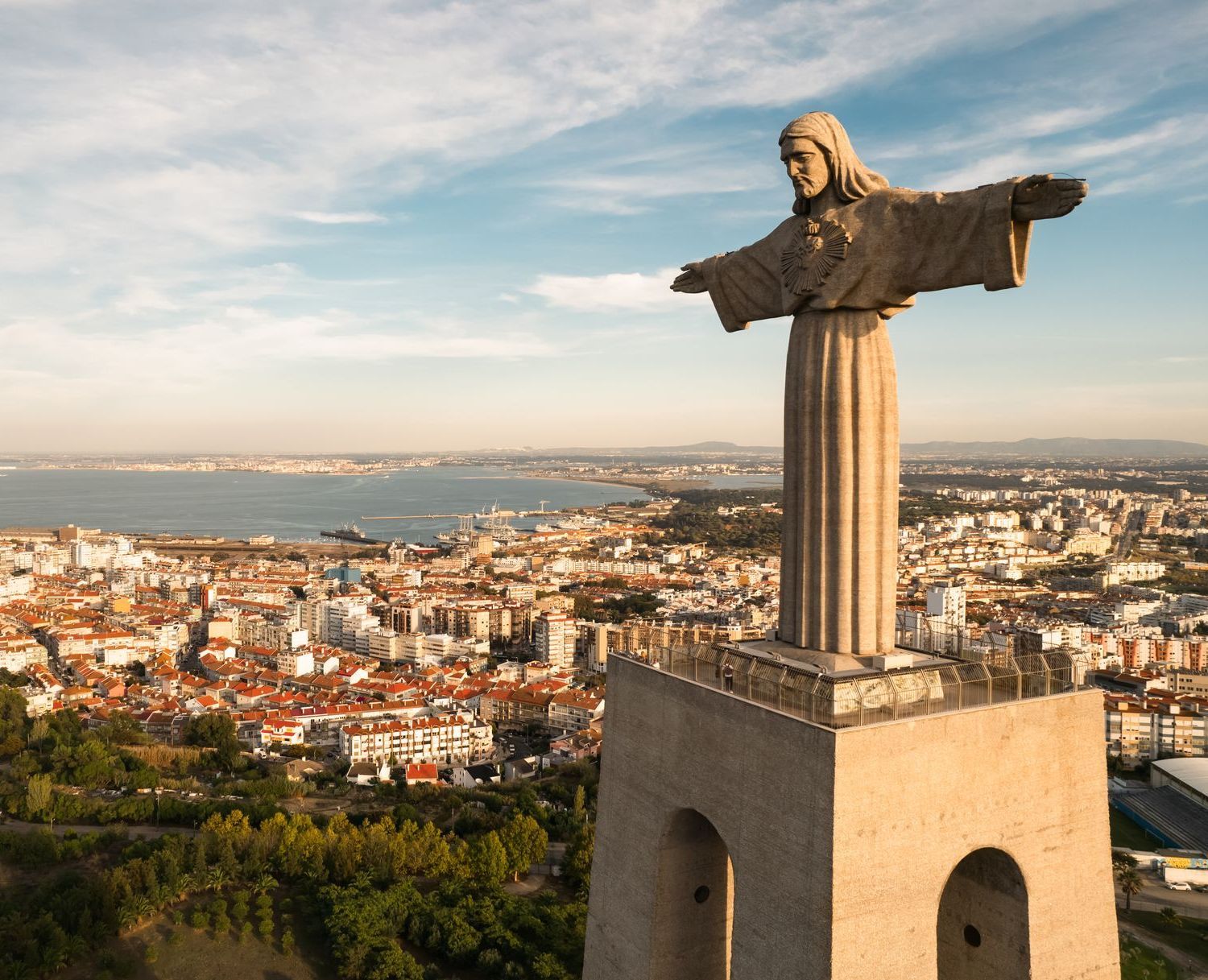 A statue of jesus is standing on top of a building overlooking a city.