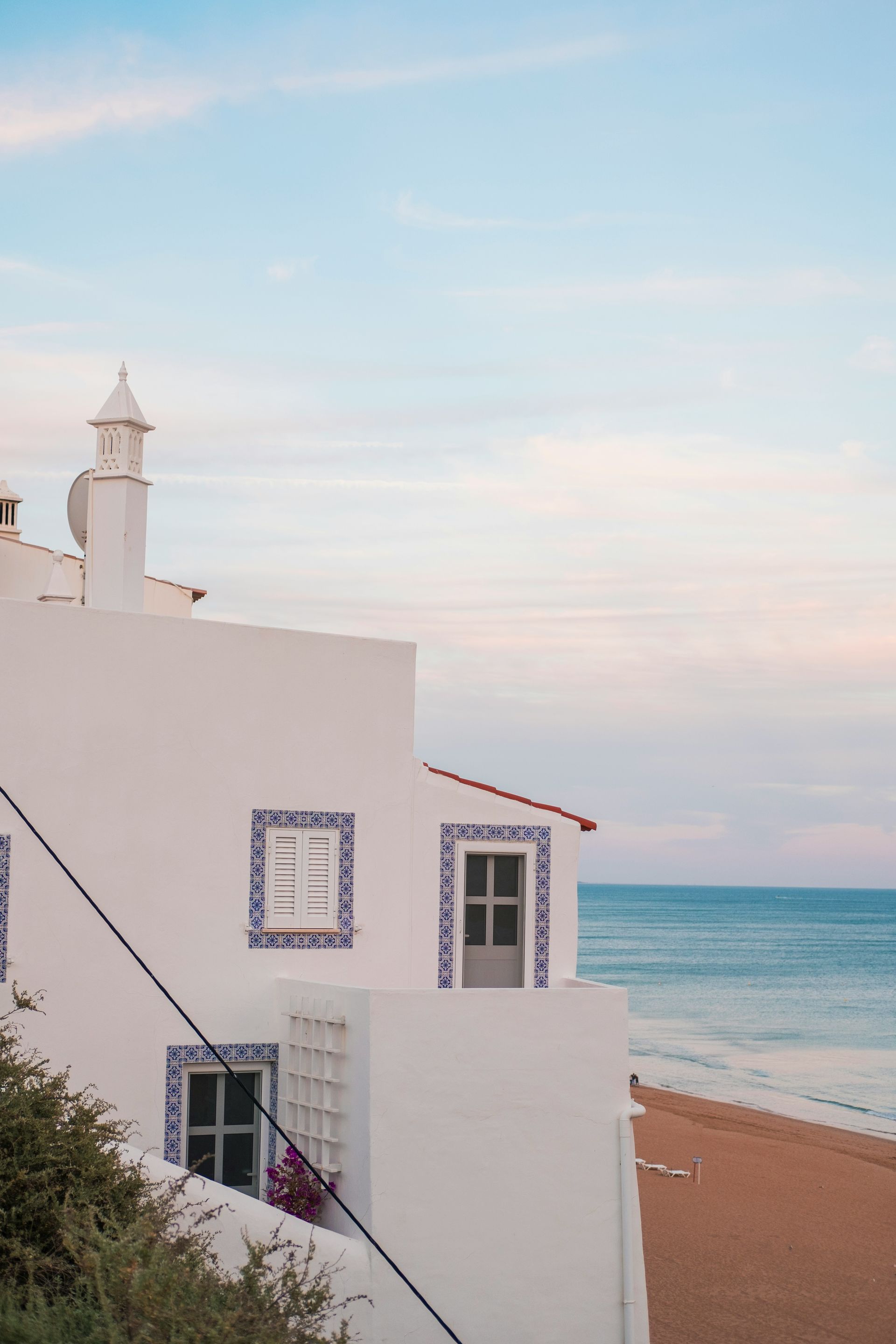 A white building with blue tiles on the side is next to a beach.