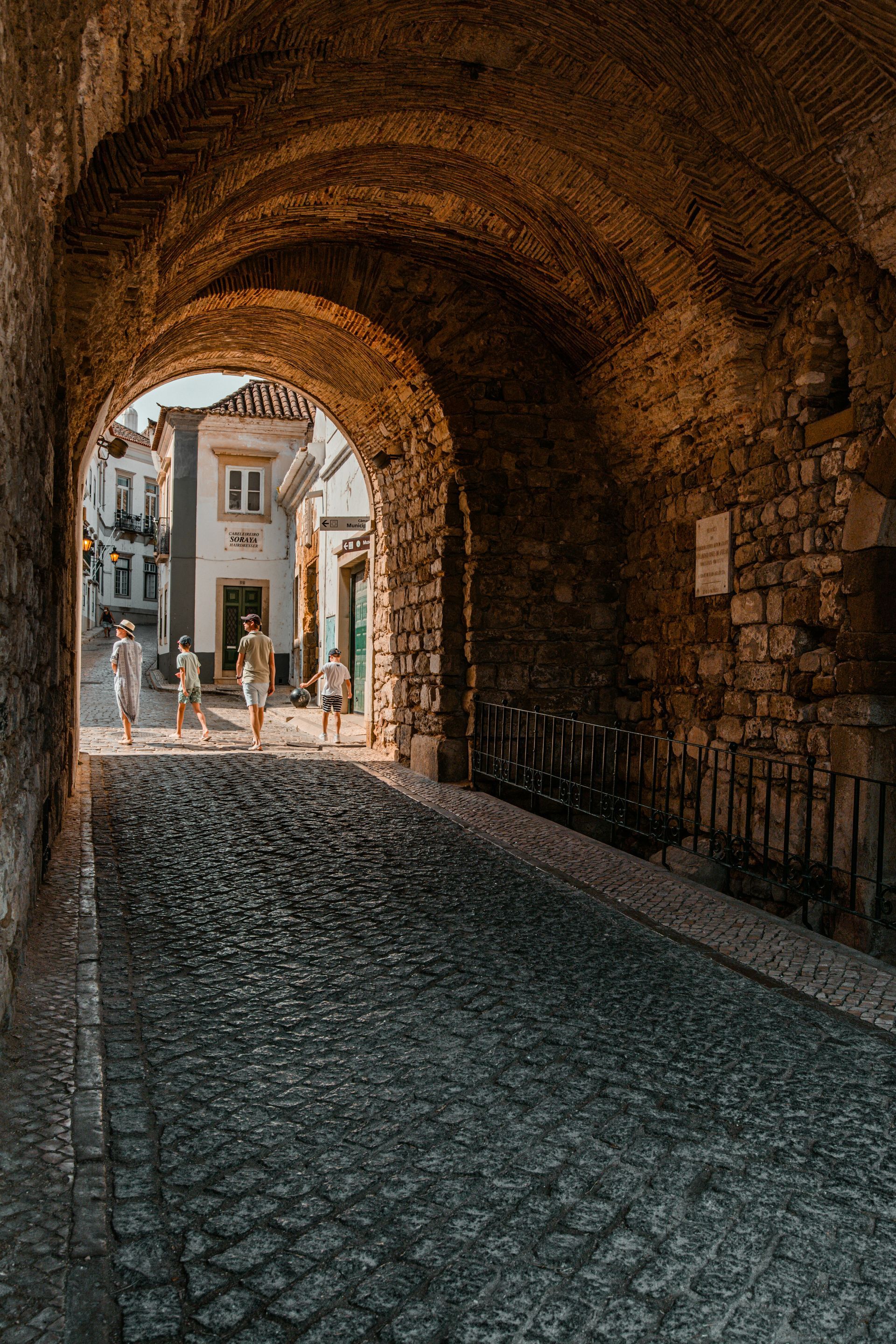 A stone archway leading to a cobblestone street in a small town.