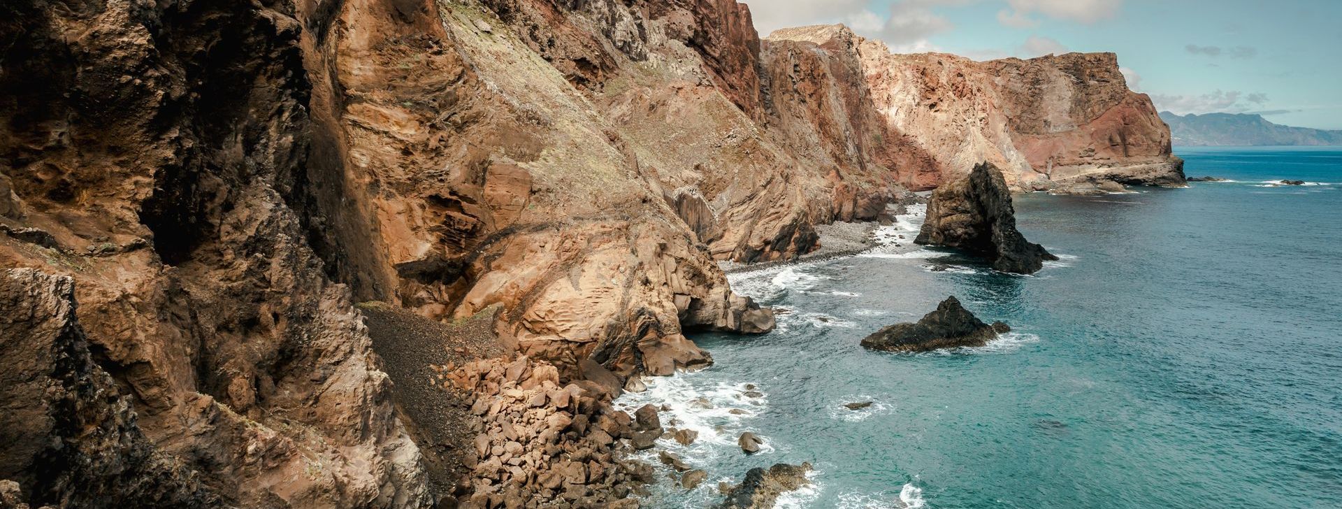 A cliff overlooking the ocean with waves crashing on the rocks.