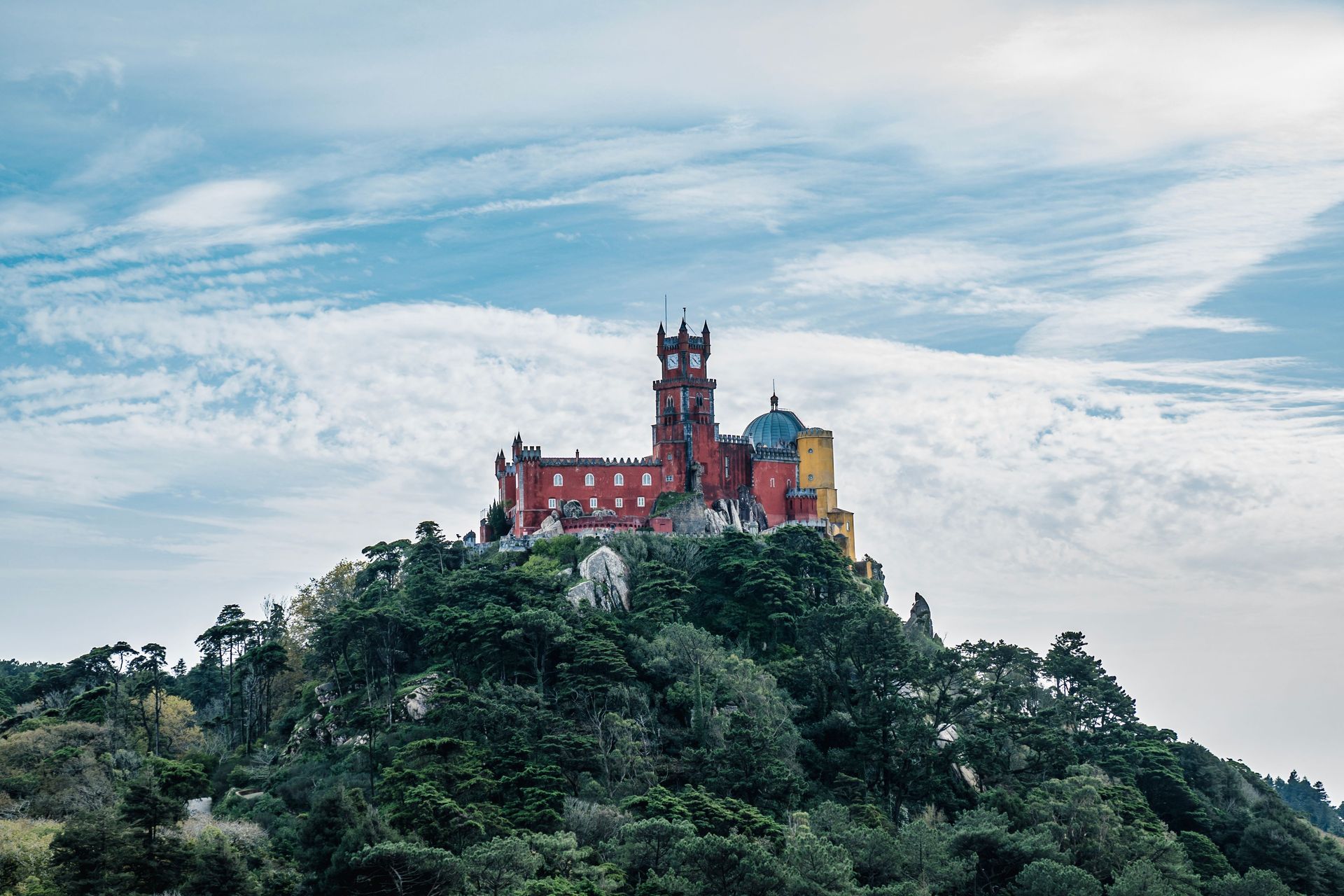 A colorful castle is sitting on top of a hill surrounded by trees.