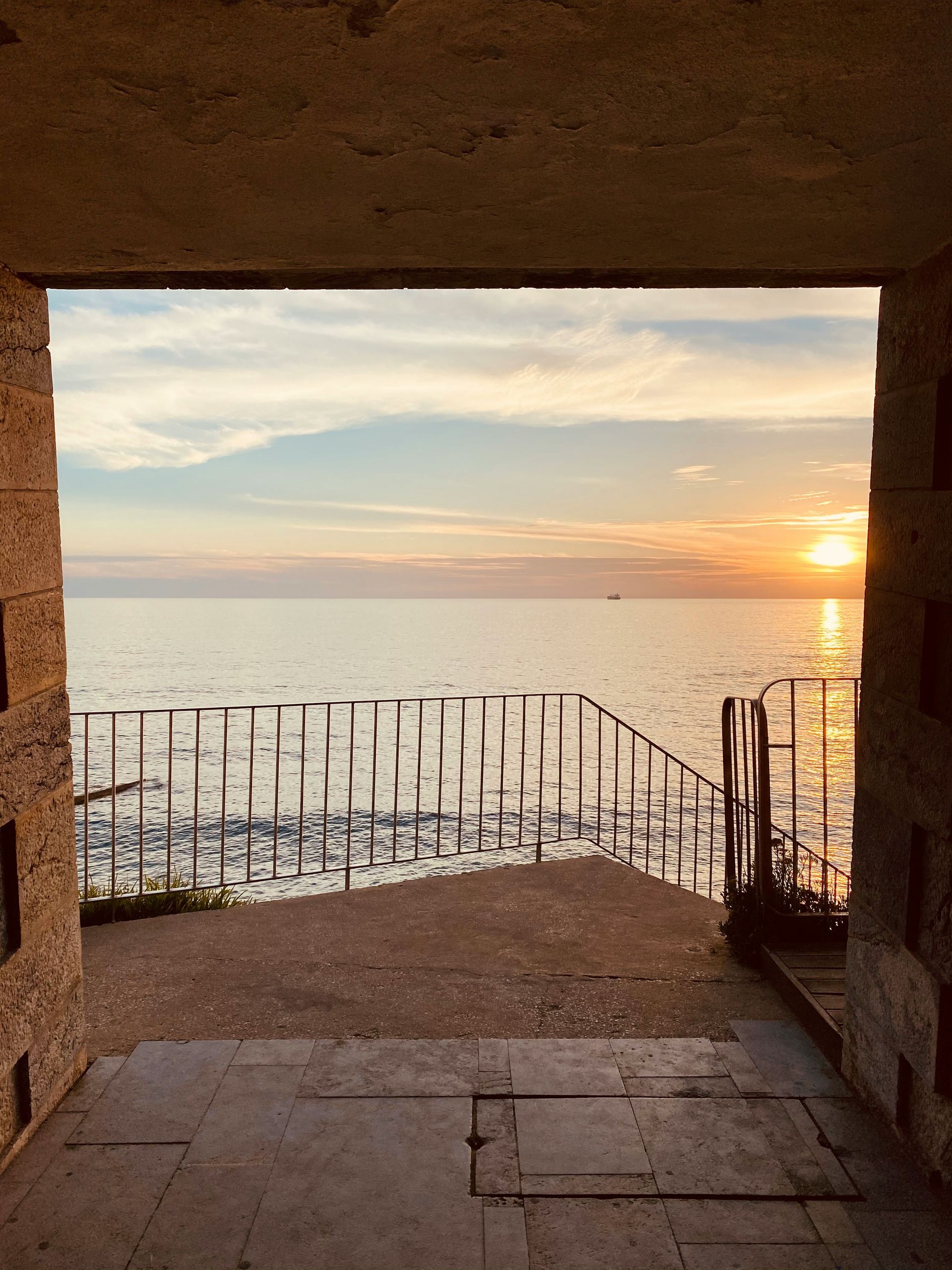 A sunset over the ocean is seen through a doorway