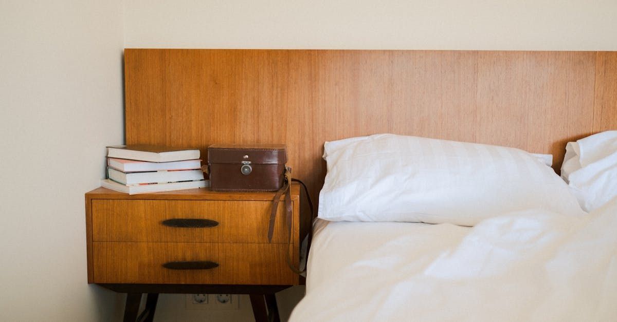 A bed with white sheets and a wooden headboard next to a nightstand.