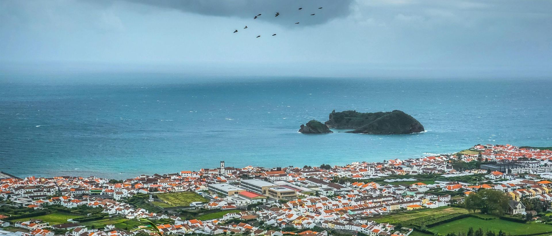 An aerial view of a city and a small island in the middle of the ocean.