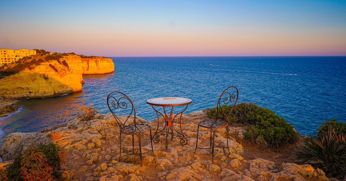 A table and chairs on a rocky cliff overlooking the ocean.