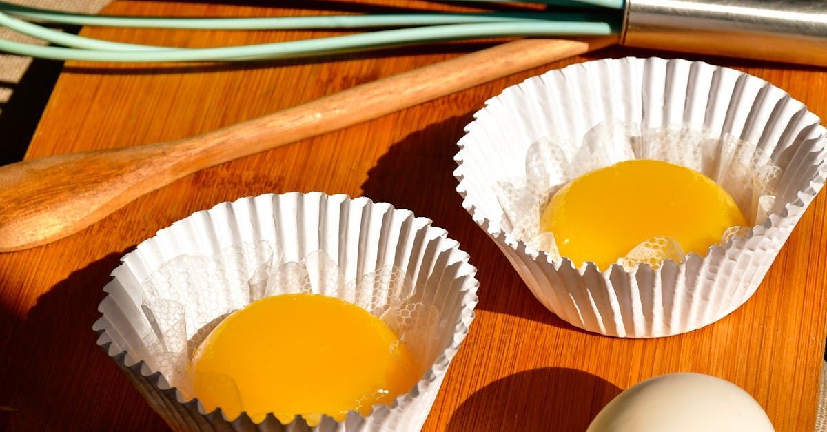 Two cupcake liners with eggs in them on a wooden table.