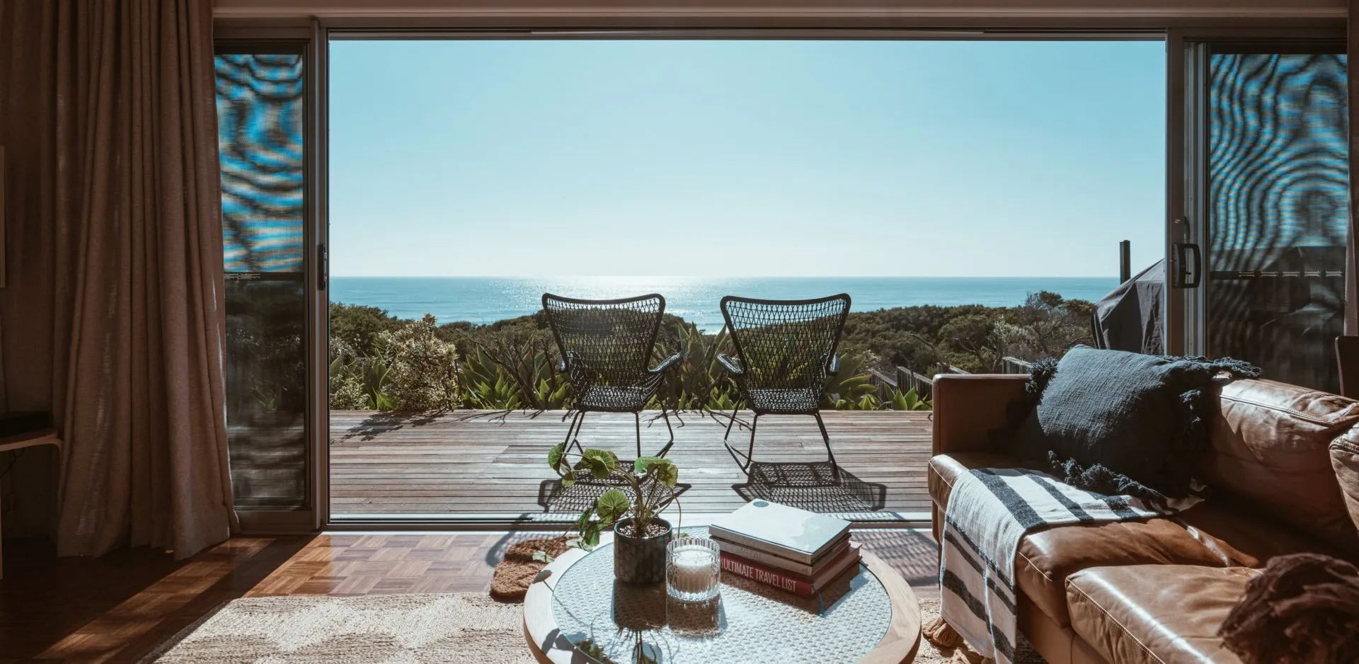 A living room with a couch , table and chairs and a view of the ocean.