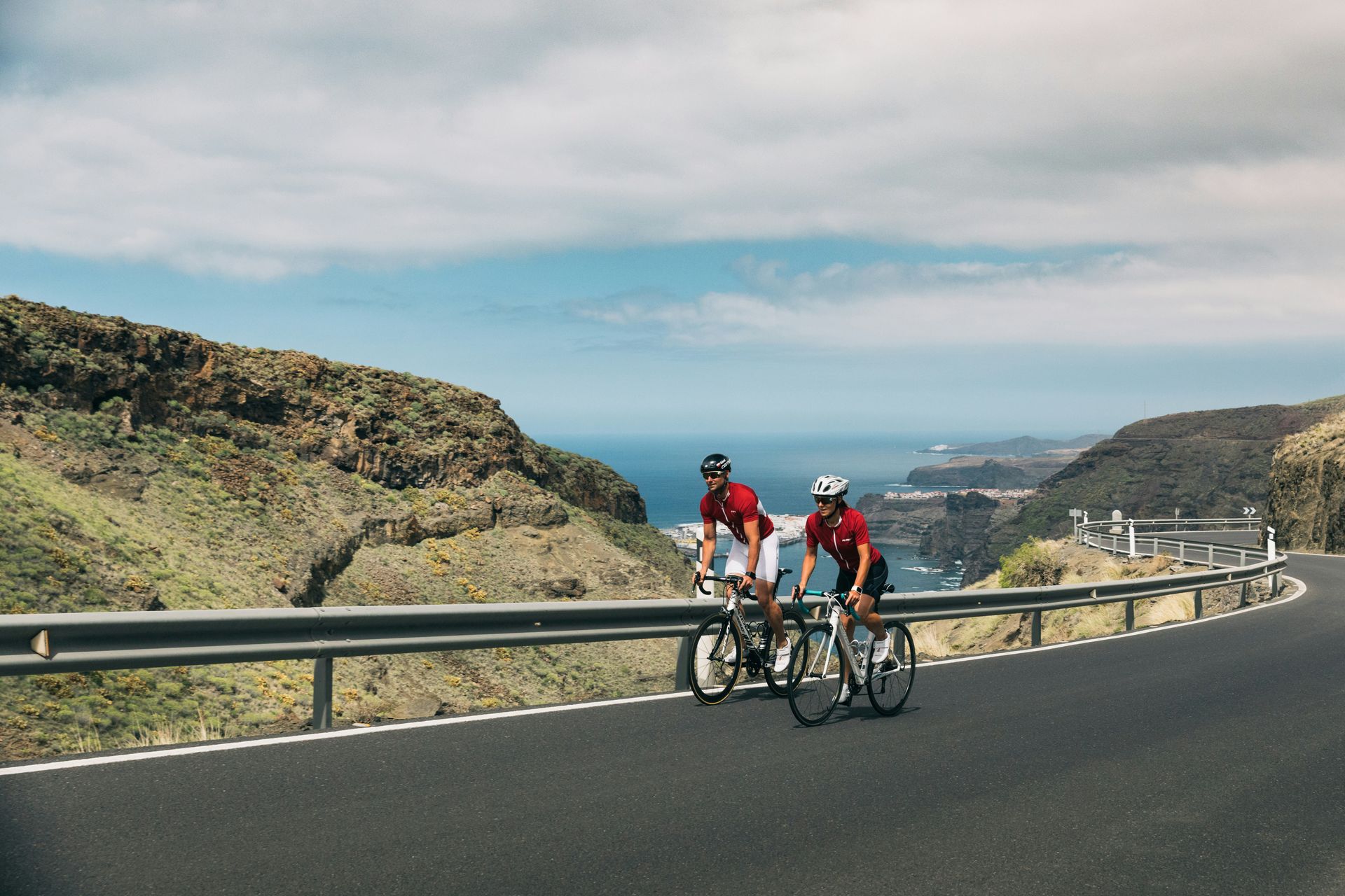 Two people are riding bicycles down a mountain road.