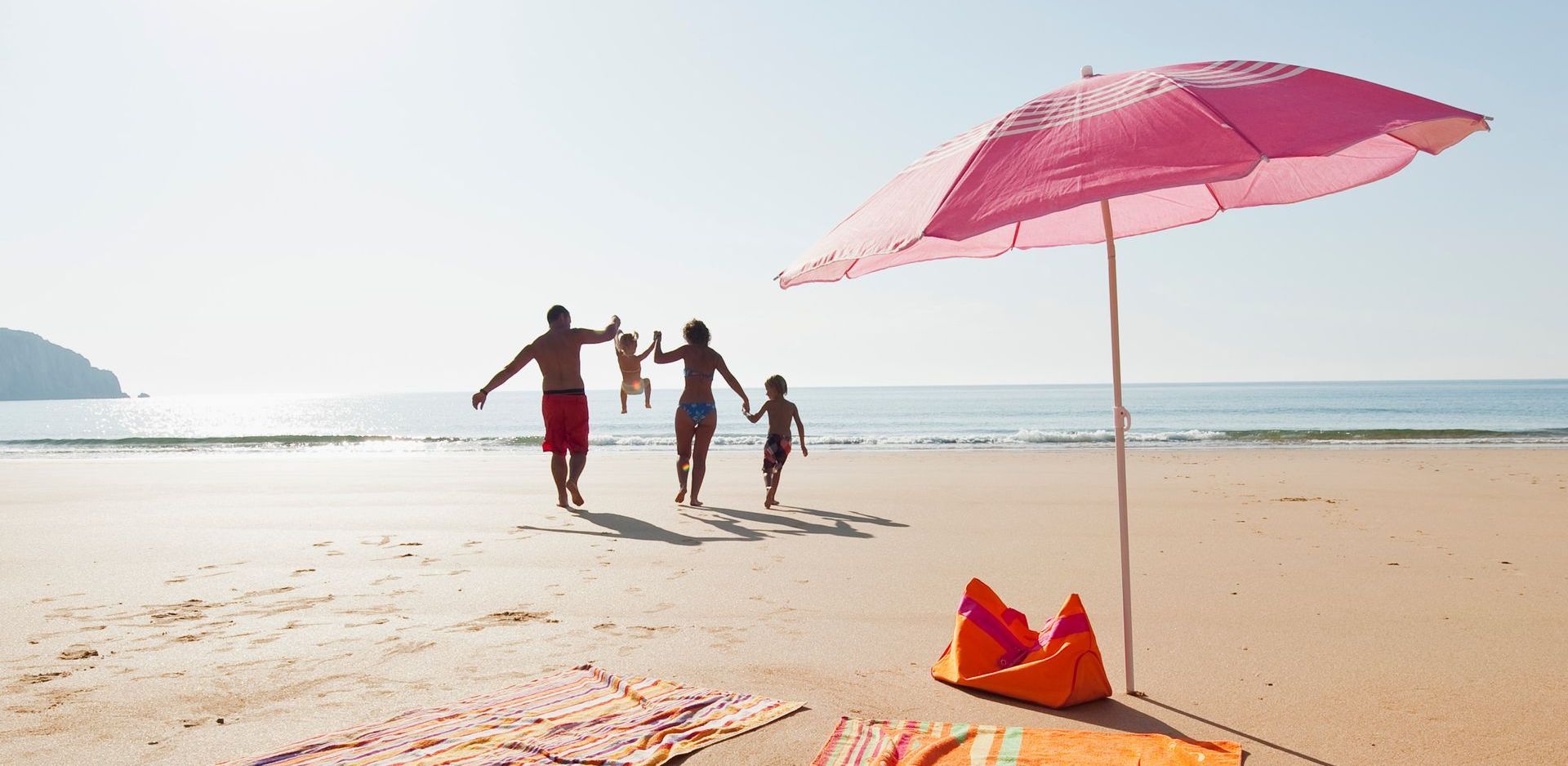 A family is walking on the beach holding hands under an umbrella.