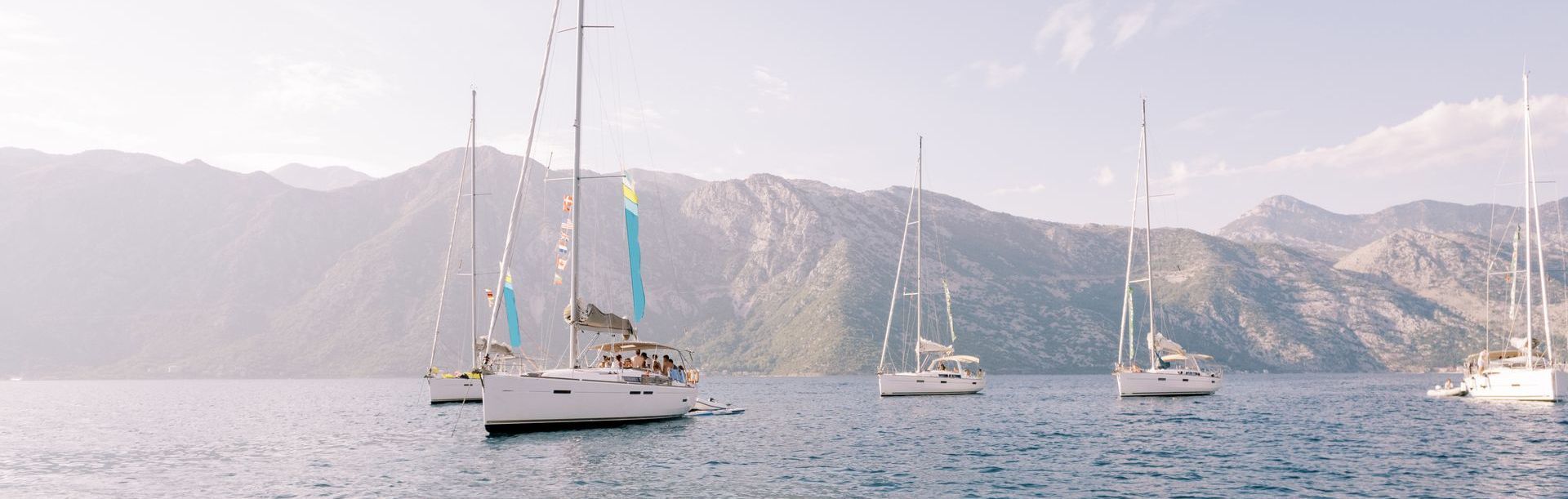 A group of sailboats are floating on top of a body of water with mountains in the background.