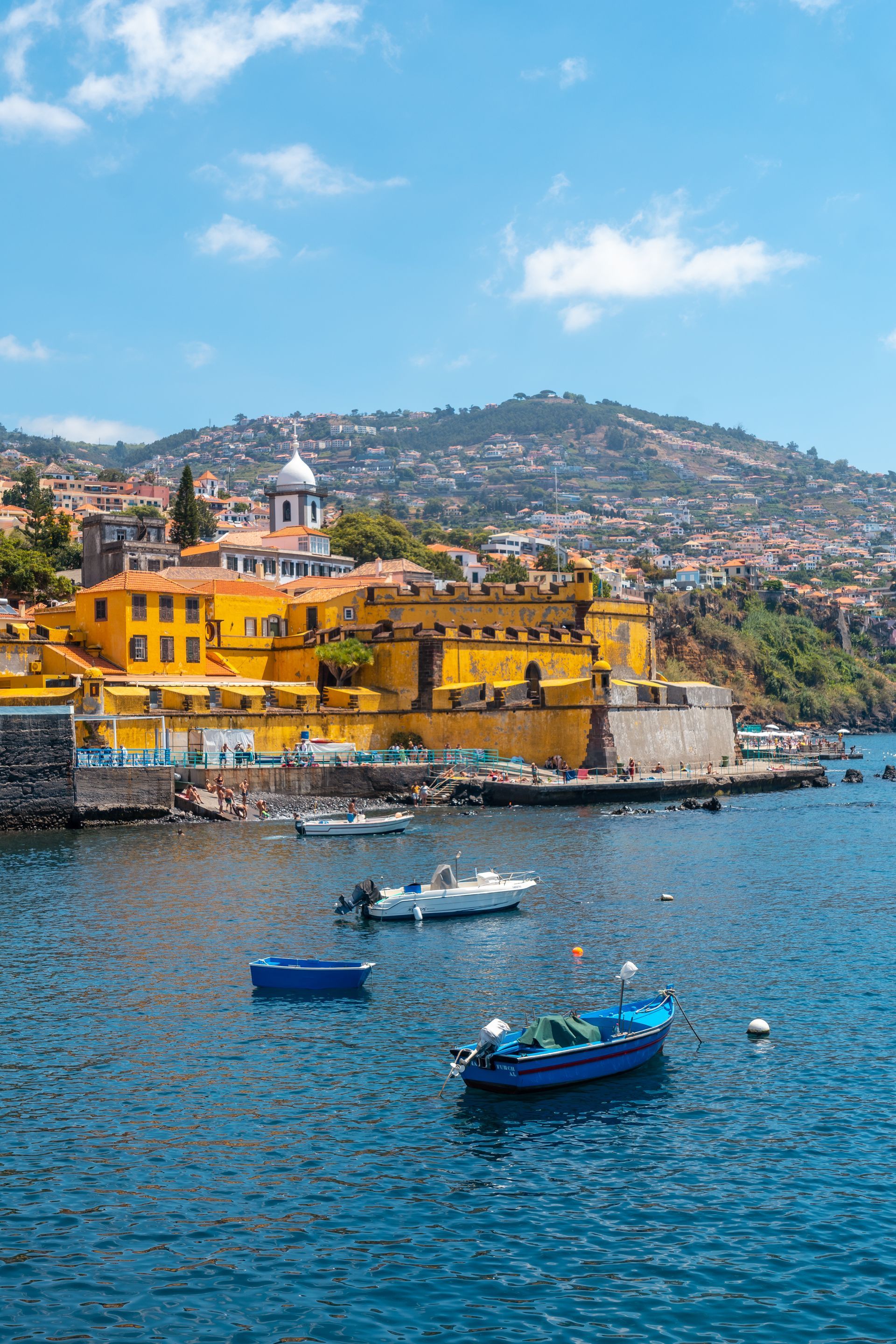 boats are floating in the water near a yellow building funchal vacation properties