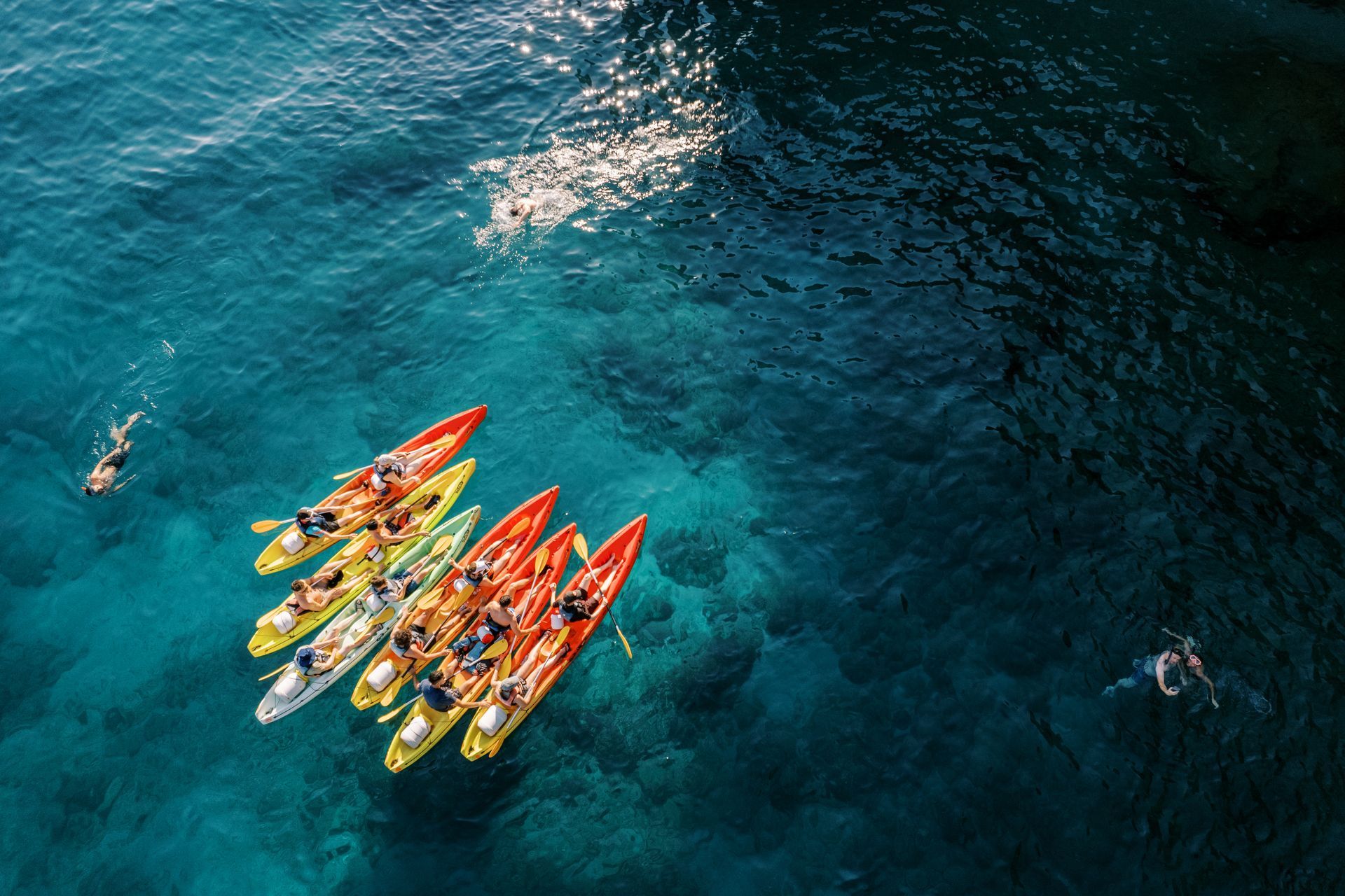 A group of people are rowing kayaks in the ocean.