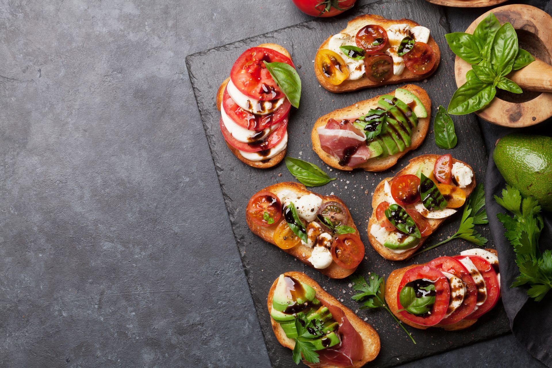 A slate cutting board topped with a variety of sandwiches.