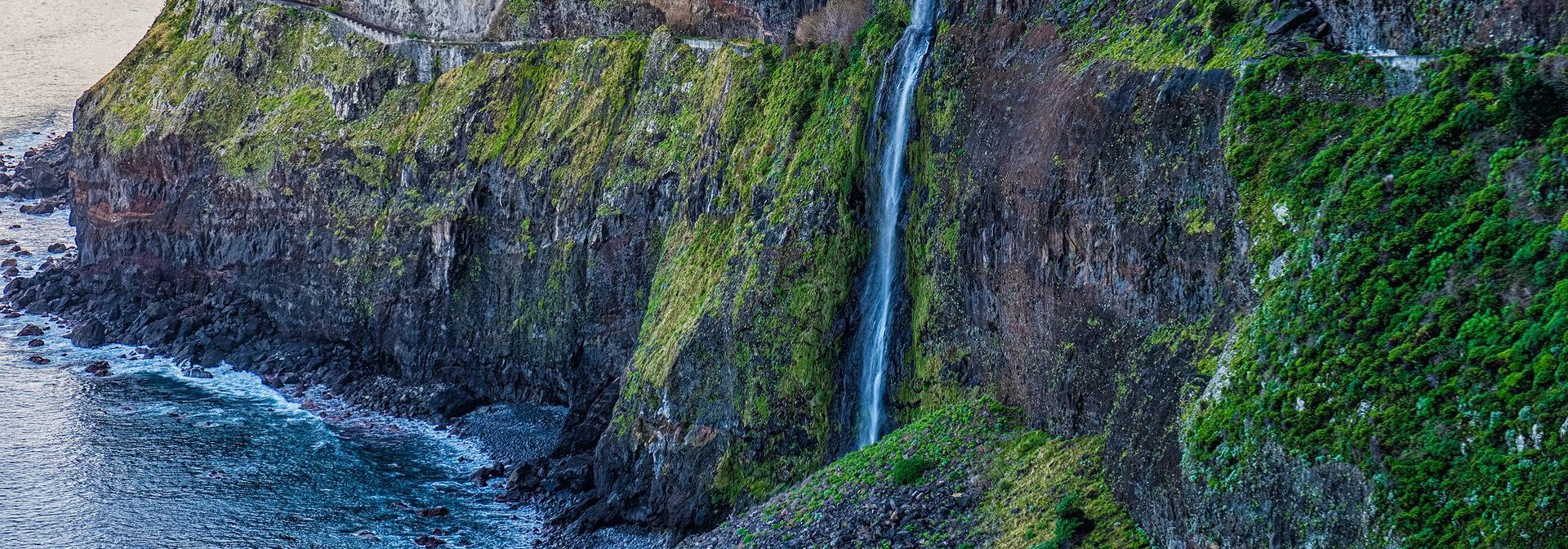 An aerial view of a waterfall on a cliff overlooking the ocean.