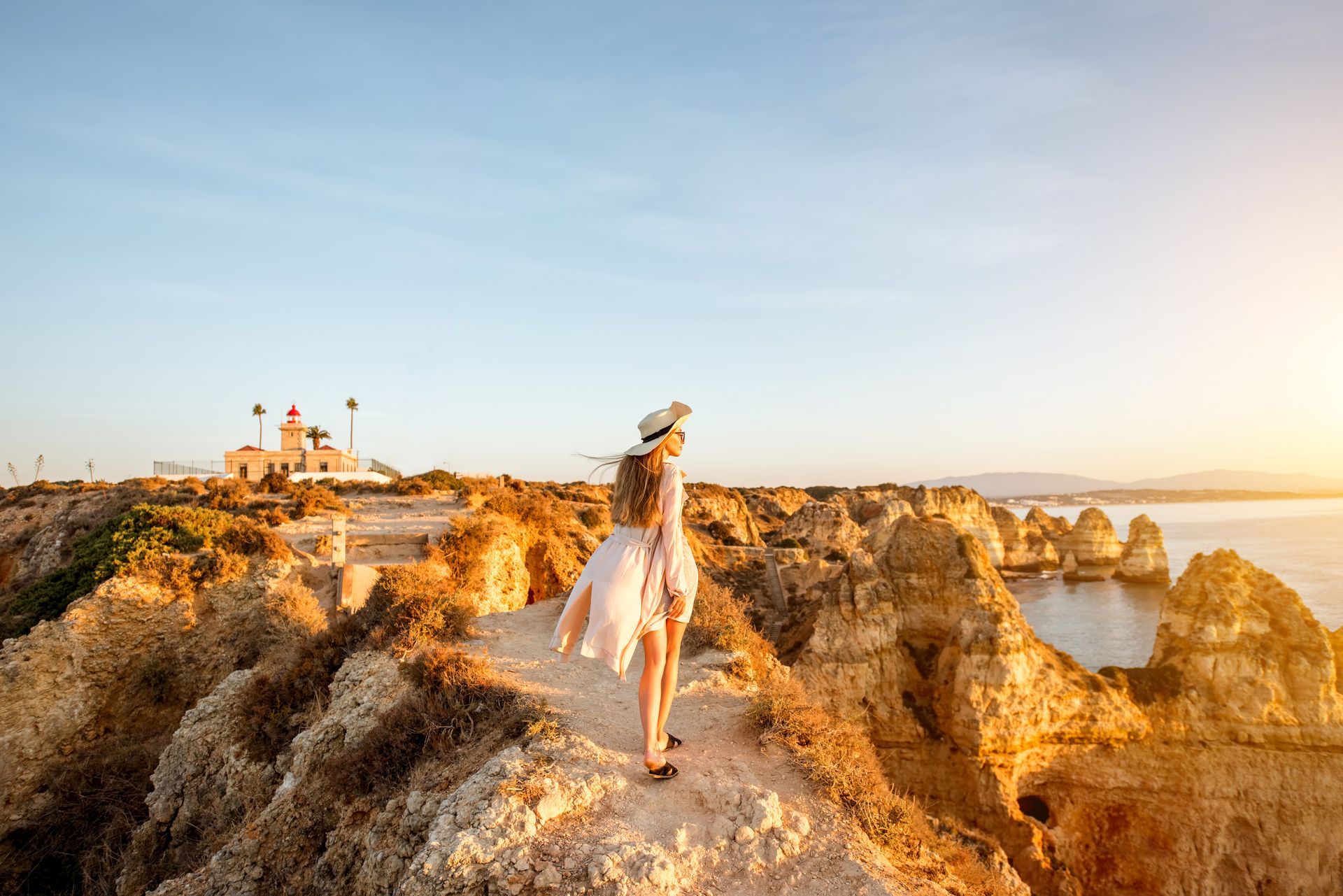 A woman is standing on top of a rocky cliff overlooking the ocean.