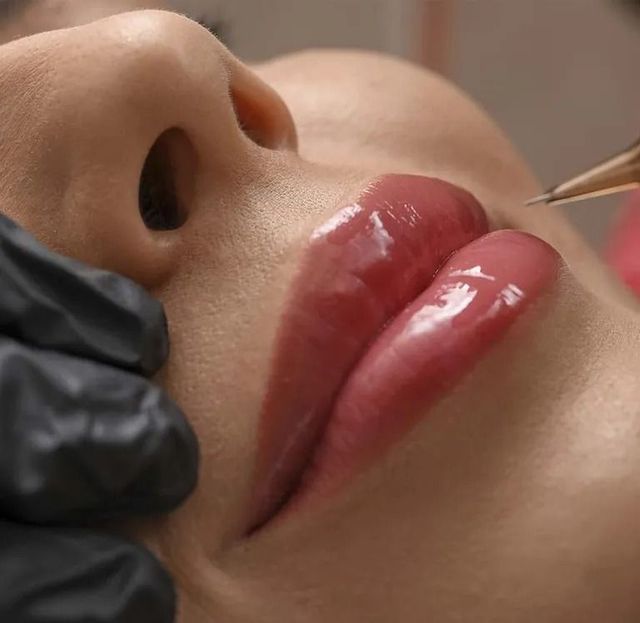 Persona ruborizándose los labios, primer plano. Labios rosados y brillantes. Mano enguantada en negro.