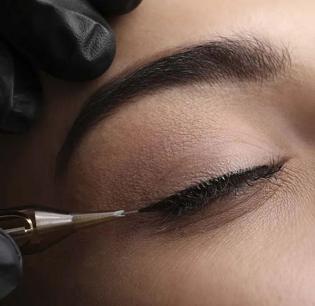 Procedimiento de maquillaje permanente con delineador de ojos que se realiza en el ojo de una persona, con una mano enguantada sosteniendo un lápiz para tatuar.