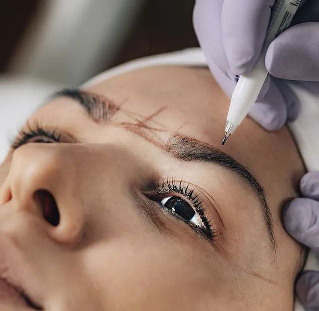 Persona que recibe microblading de cejas; el artista dibuja líneas guía con un bolígrafo.