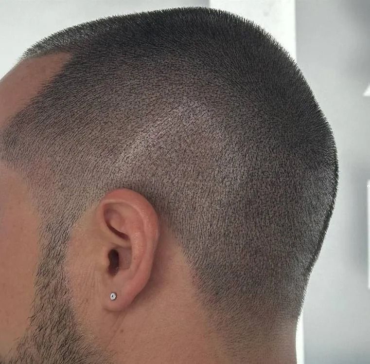 Hombre con pelo corto y descolorido. Vista de perfil, barba incipiente y pendiente pequeño.