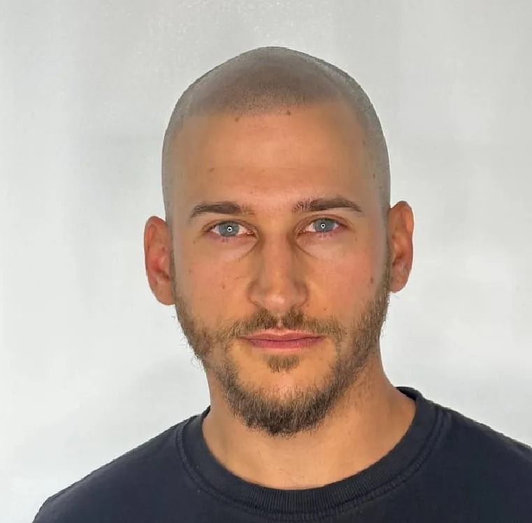 Hombre con cabello corto y rapado y barba, mirando a la cámara.