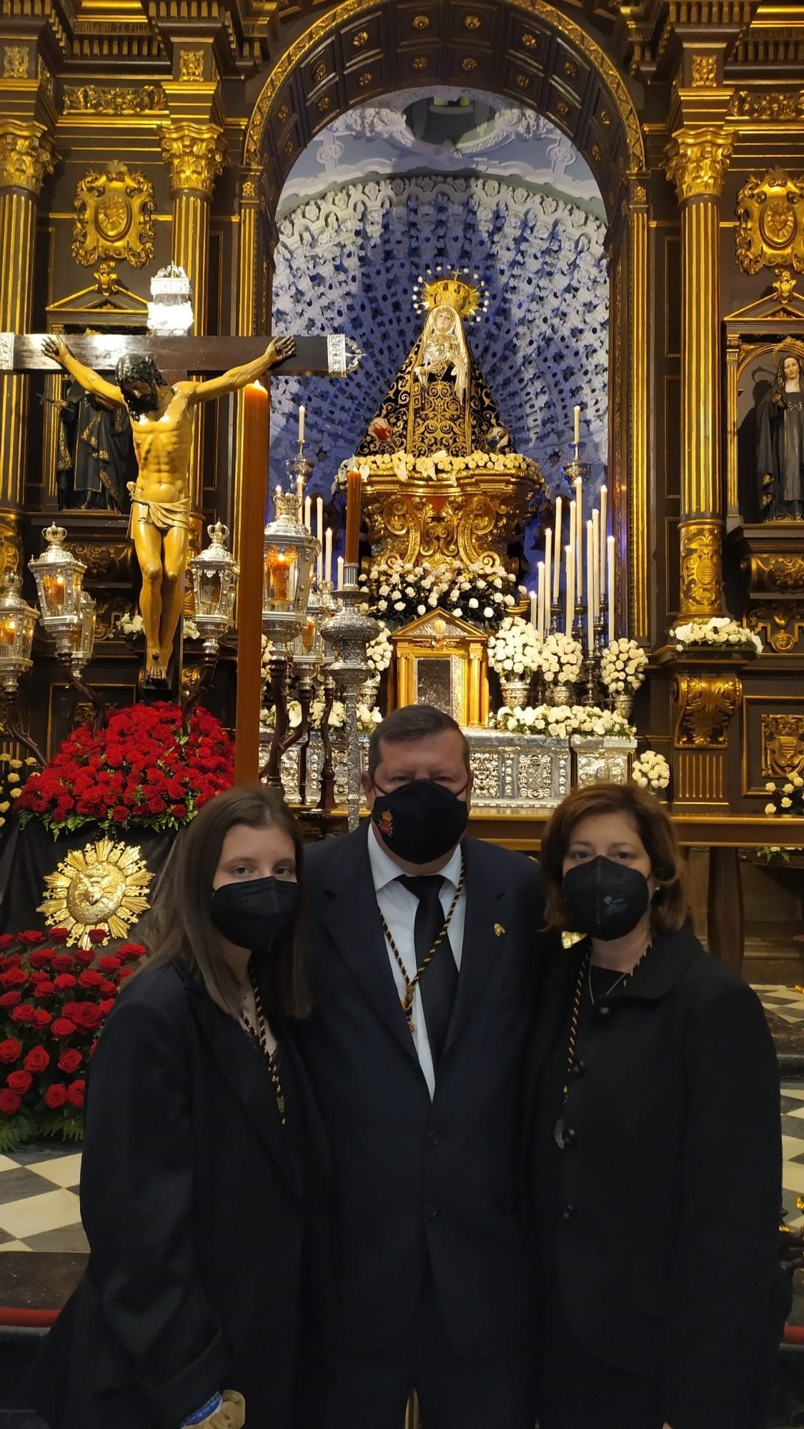 Un hombre y dos mujeres con máscaras faciales posan para una foto frente a un altar en una iglesia.