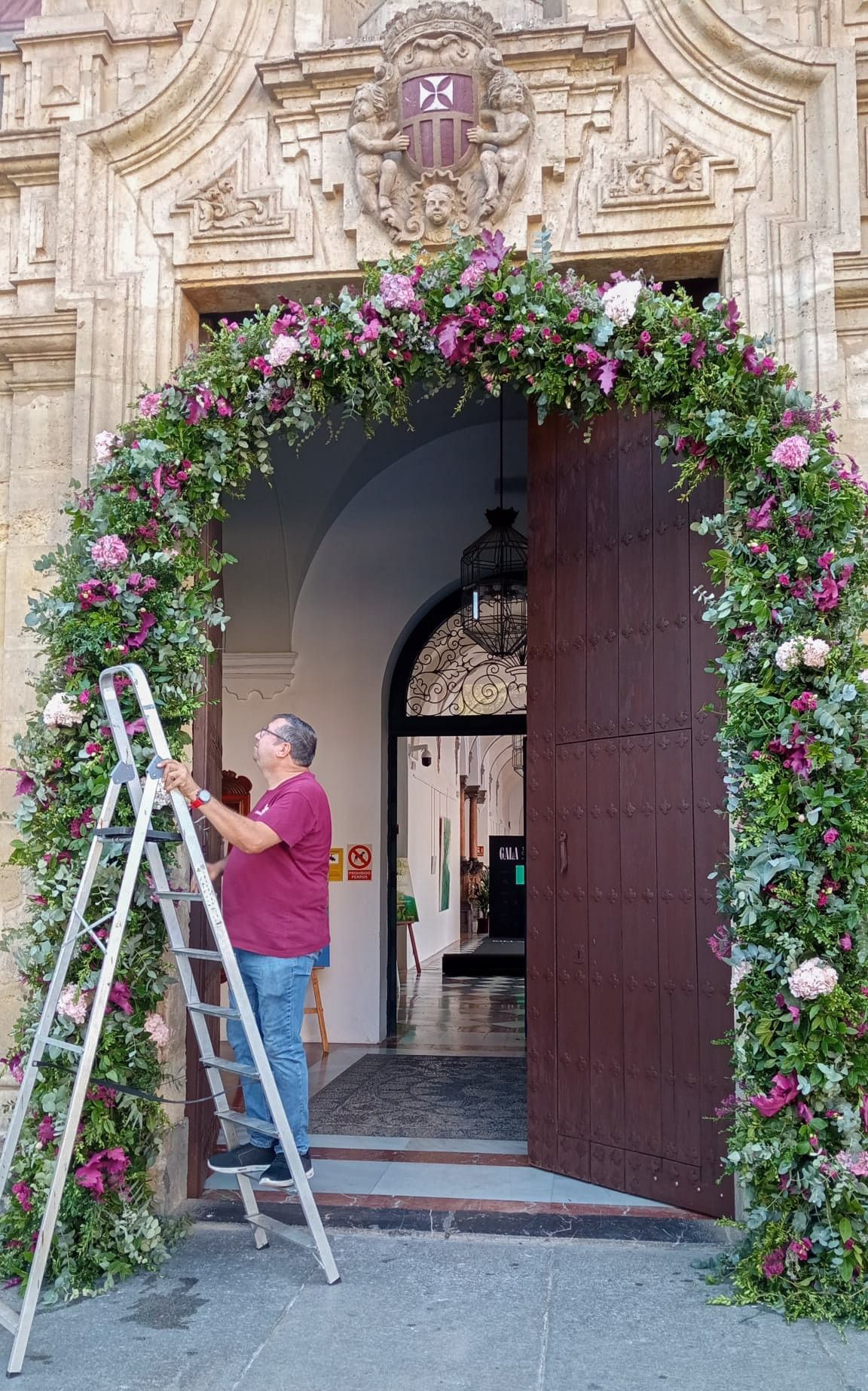 Un hombre está de pie en una escalera frente a una puerta decorada con flores.