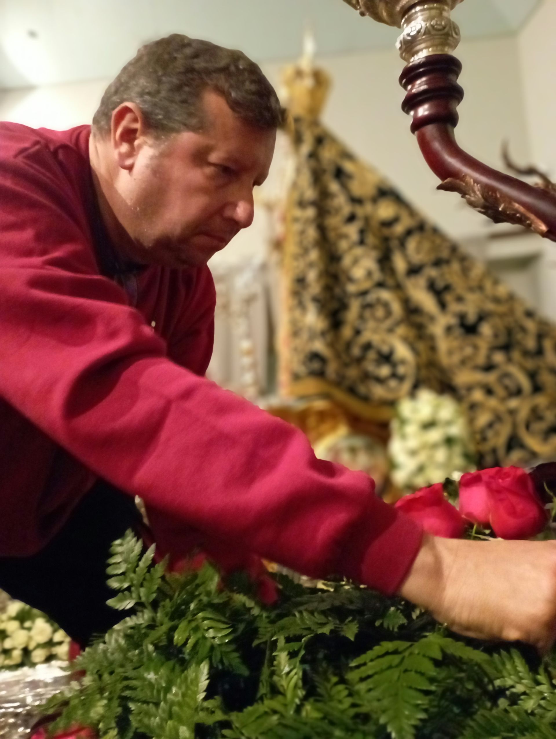Un hombre con una camisa roja está arreglando flores en una mesa.