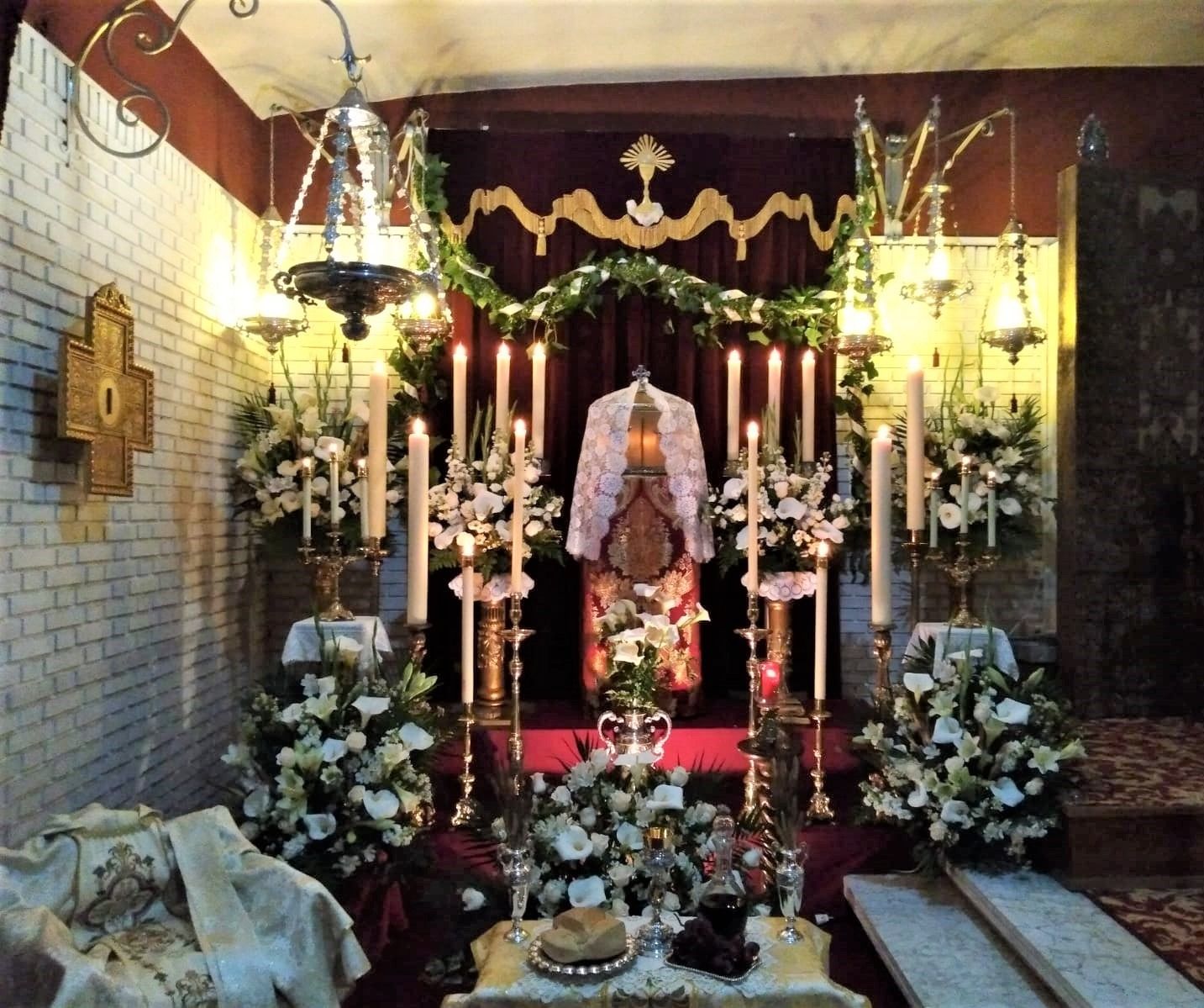 Una iglesia con velas y flores y una cruz en la pared.