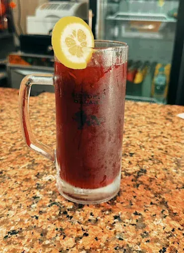 Vaso alto de bebida roja con una rodaja de limón sobre una encimera de granito.