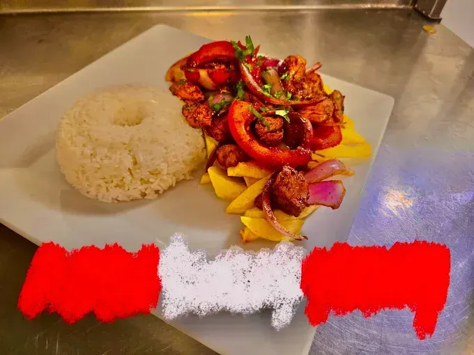 Plato peruano de Lomo Saltado con arroz, papas fritas y carne y verduras salteadas, con una bandera peruana borrosa.