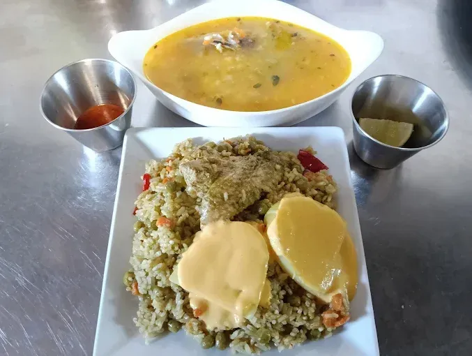 Comida de arroz, sopa y salsas sobre una mesa de metal, con un tazón de sopa blanco en el fondo.