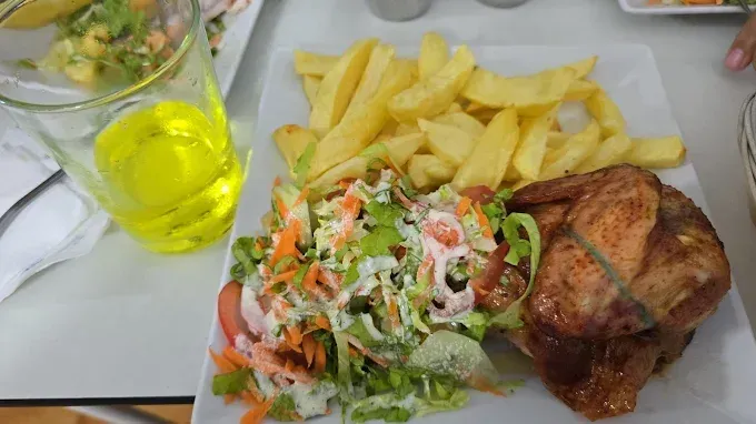 Plato con pollo asado, patatas fritas y ensalada; a su lado hay un vaso de líquido amarillo.