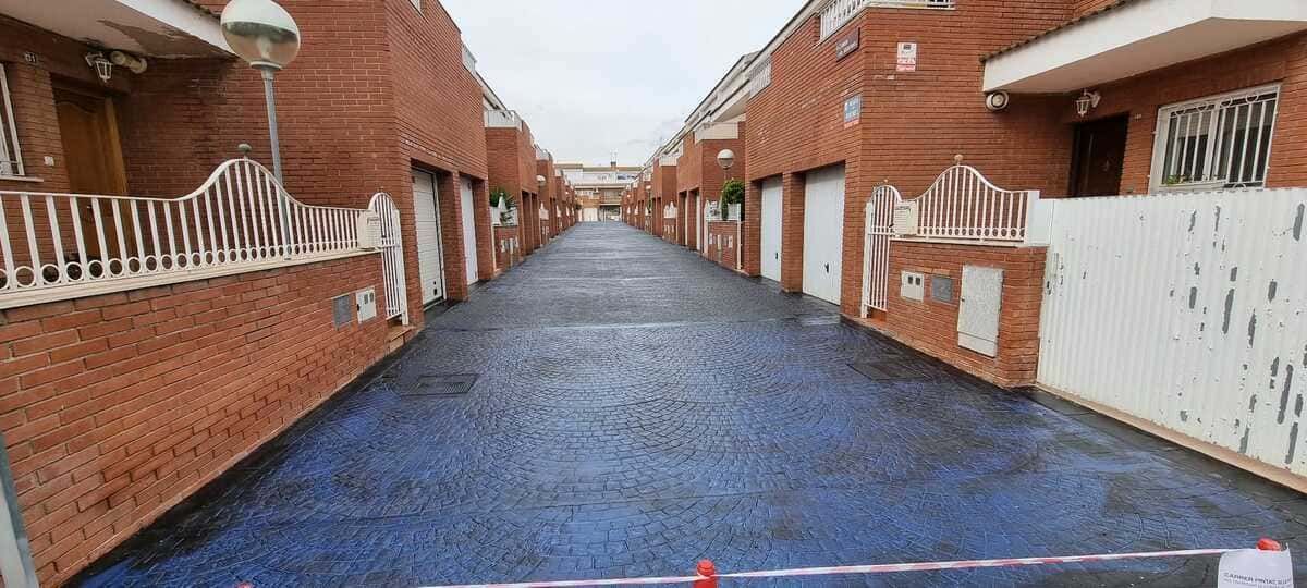 Un largo callejón de casas adosadas de ladrillo rojo con puertas y garajes blancos. La calle es azul.