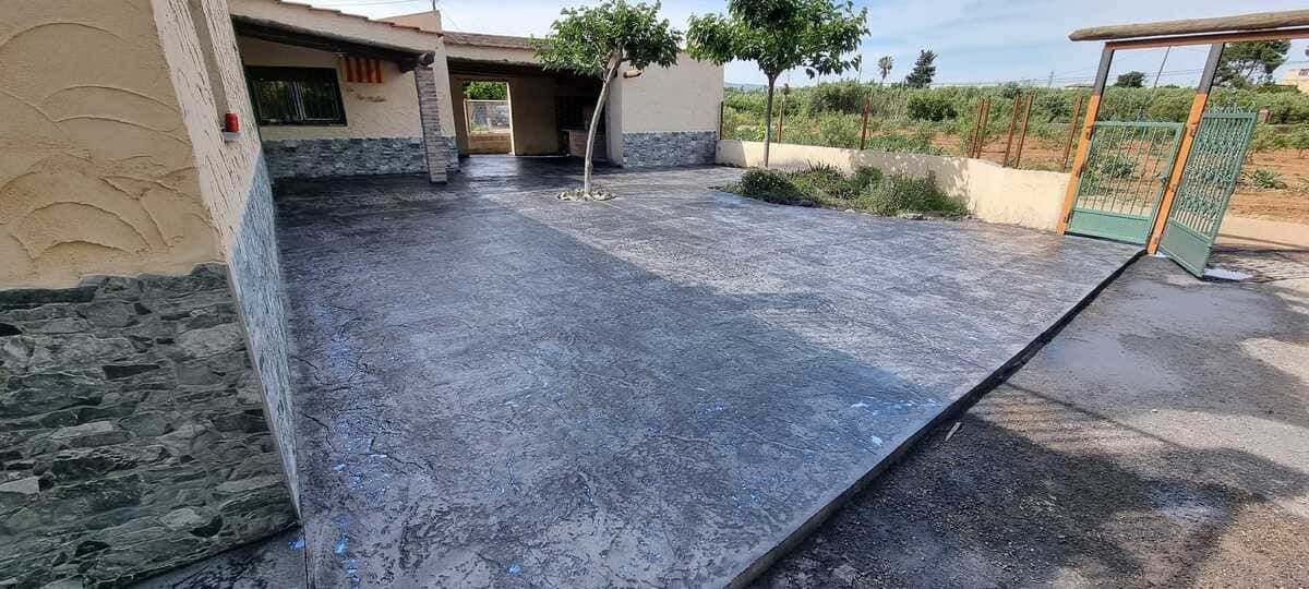 Un patio pavimentado con un edificio al fondo y una puerta en el lado derecho.