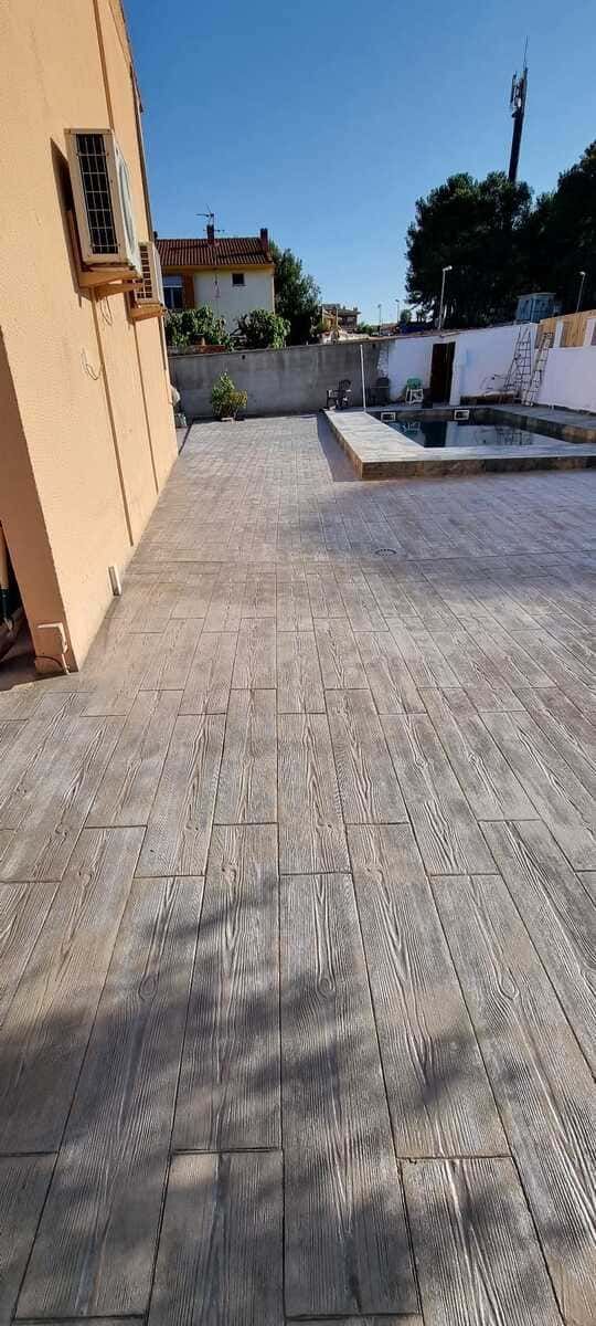 Vista exterior de un patio pavimentado junto a un edificio y piscina, bajo un cielo azul claro.