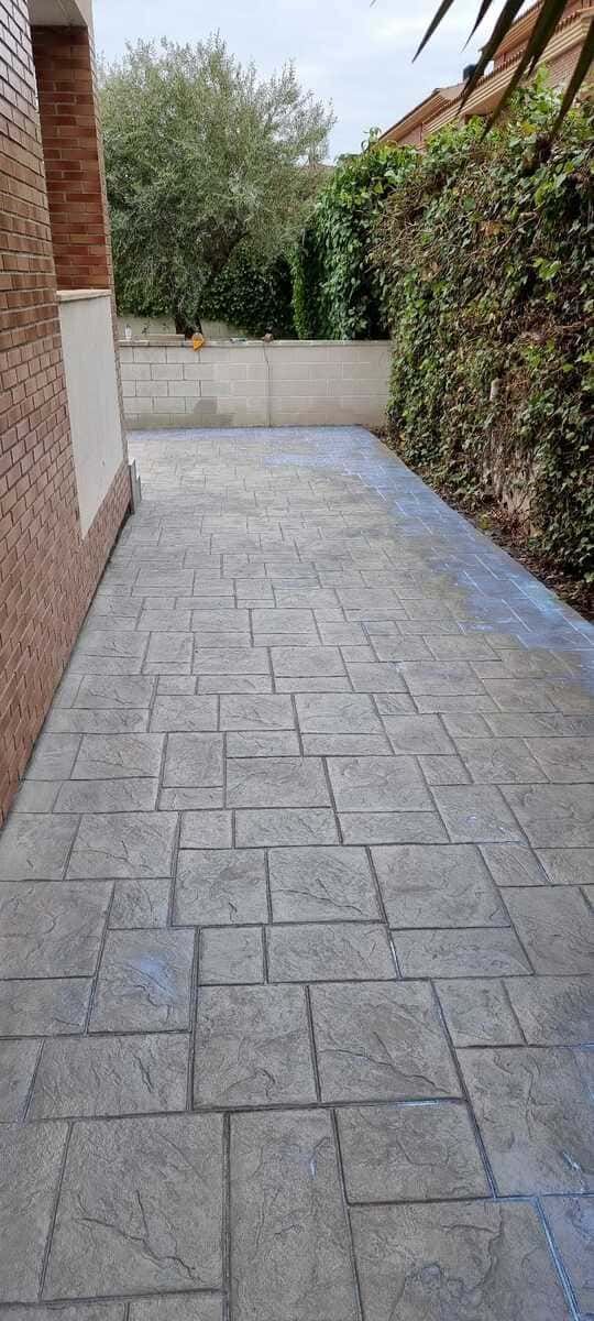 Una estrecha pasarela de hormigón con un muro de ladrillos a la izquierda y un seto a la derecha.