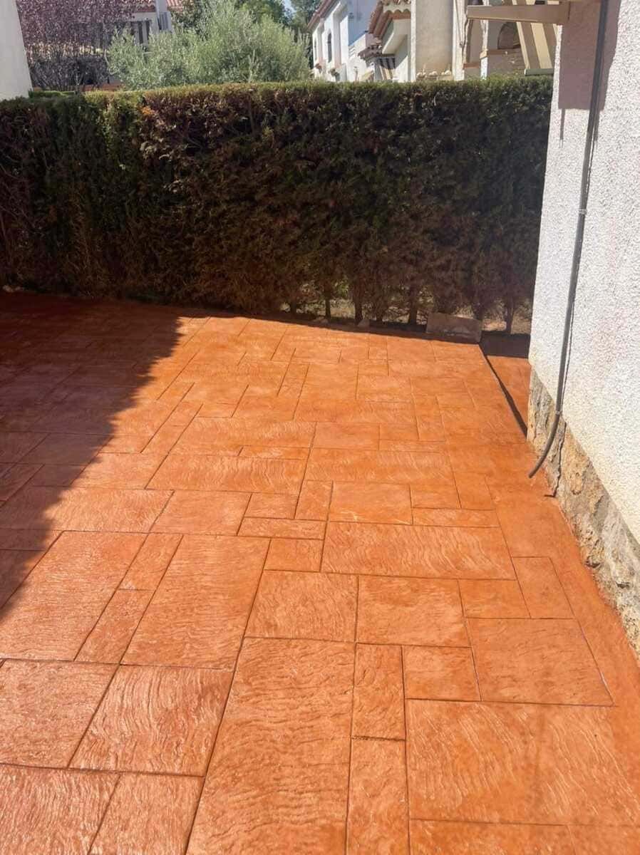Patio de hormigón estampado de color naranja con seto verde como fondo.