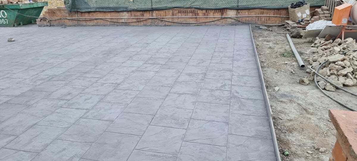 Un patio pavimentado con baldosas cuadradas, con escombros de construcción a los lados.