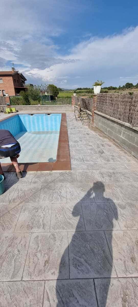 Una persona cerca de una piscina vacía al aire libre. El suelo es de hormigón impreso. Día soleado.