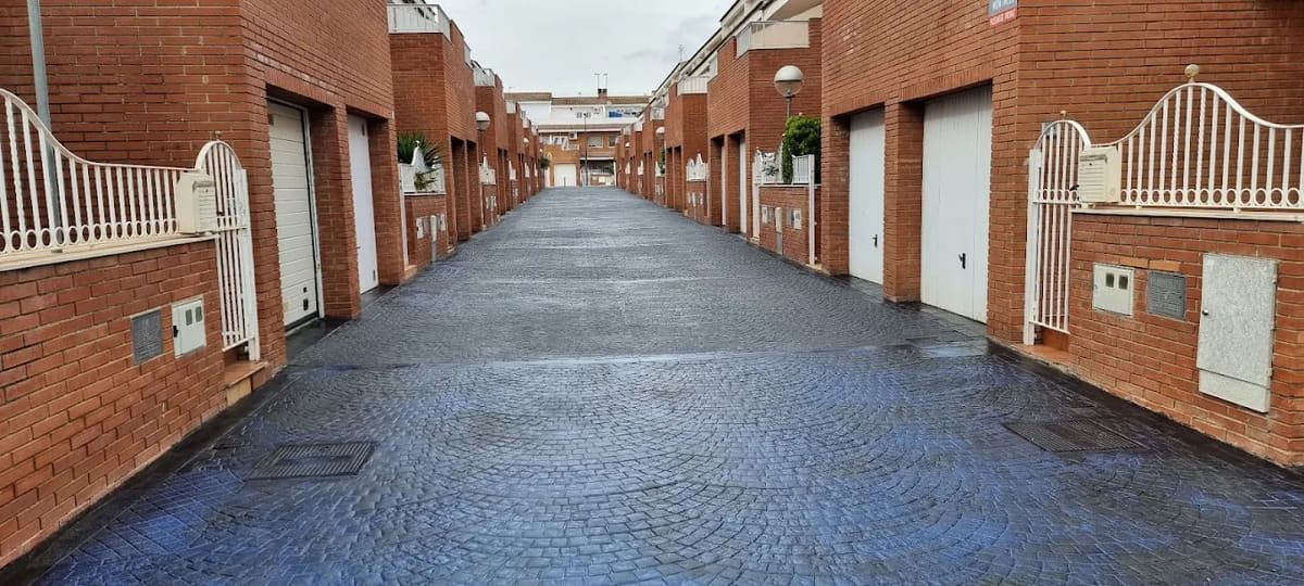 Un callejón de casas adosadas con puertas de garaje blancas cerradas, exteriores de ladrillo y pavimento azul oscuro.
