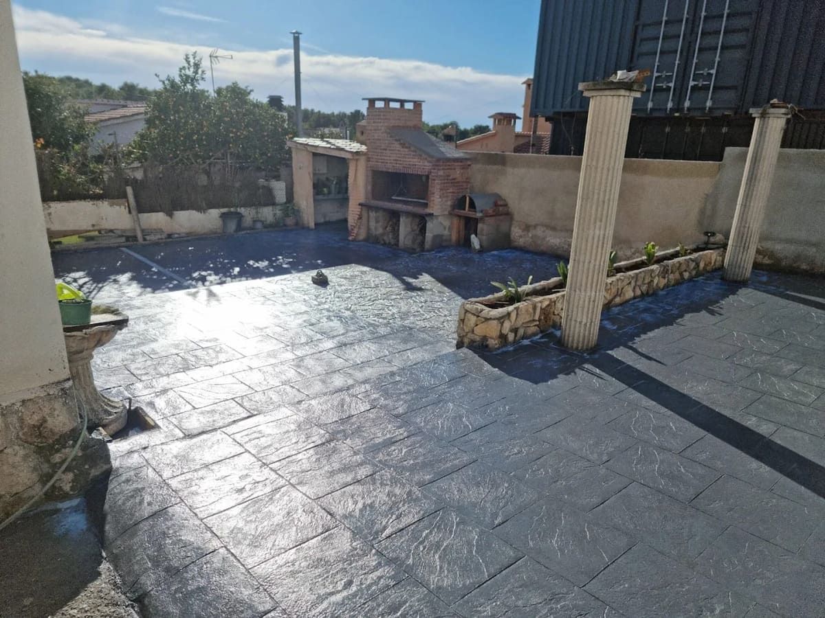 Patio al aire libre con suelo con dibujos oscuros, parrilla y pilares decorativos en un día soleado.