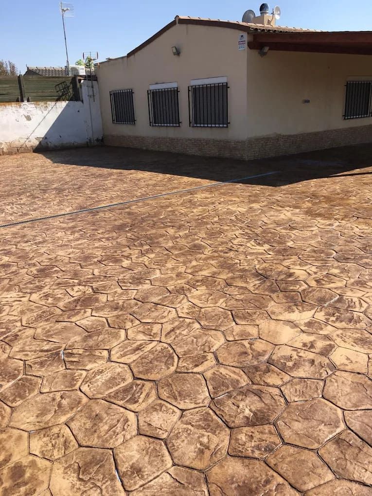 Patio de hormigón estampado de color marrón frente a una casa de color canela con ventanas enrejadas.