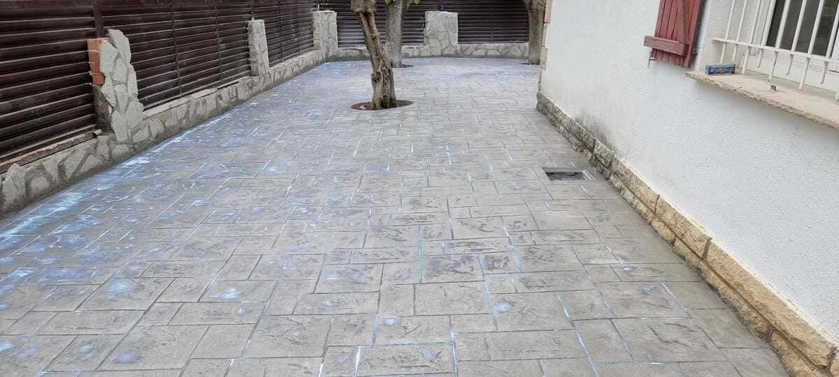 Un patio pavimentado con un árbol, una valla de madera y un edificio con una ventana.