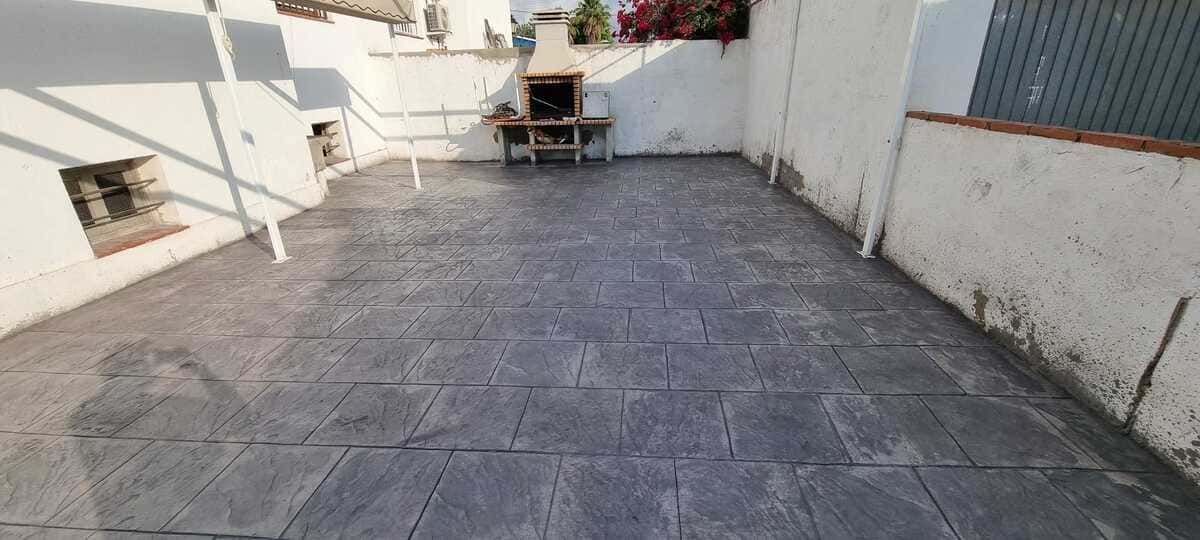 Patio con baldosas de piedra gris, paredes blancas y barbacoa de obra.