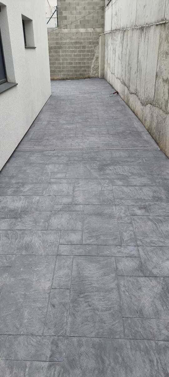 Una estrecha pasarela de piedra gris entre una pared blanca y una pared de hormigón texturizado.